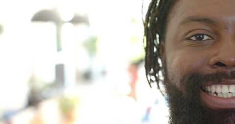 Smiling man with beard and dreadlocks looking at camera in bright high-key lobby closeup
