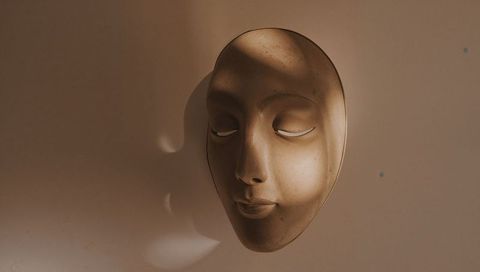 Serene sculpted face mask mounted on warm beige wall casting soft crescent shadow
