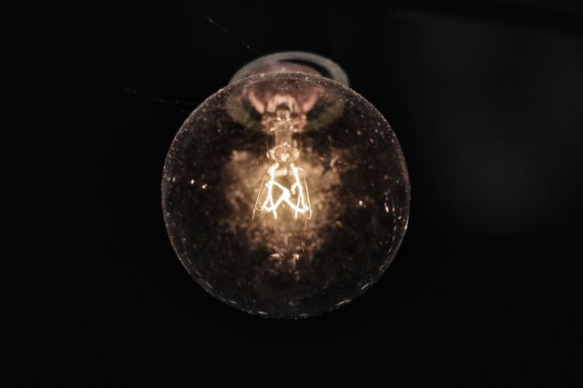 Close-up view of glowing light bulb with visible filament against dark background. Great for illustrating concepts related to energy, illumination, electricity, and innovation. Suitable for technology, science, and lighting theme advertisements or educational materials.