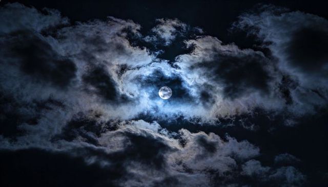 Glowing Full Moon Breaking Through Layered Clouds with Halo and Dramatic Night Sky