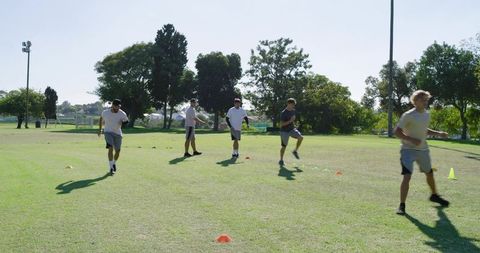 Young men doing agility drills on grass field with cones for team fitness training