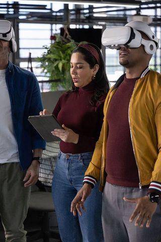 Multicultural team testing VR headsets with woman holding tablet in modern office