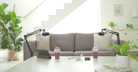 Recording podcast in bright minimal living room with microphone arms, tablet, smoothies