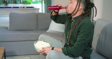 Mid-adult man with dreadlocks enjoying snack and drink on sofa during cozy movie night