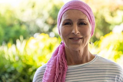 Senior woman with pink headscarf smiling in lush garden