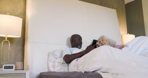 Senior Couple Relaxing in Bed Sharing Smartphone Moment