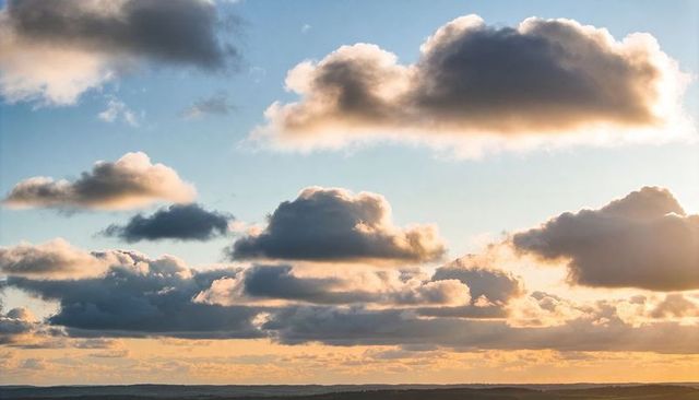 Sunlit Cumulus Clouds Over Rolling Hills at Golden Hour Dawn with Dramatic Low Light