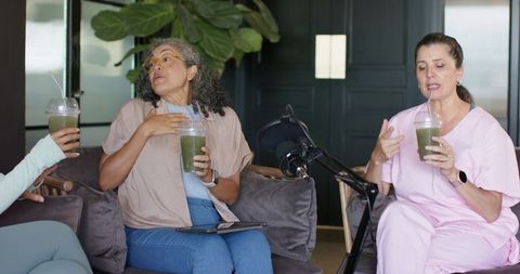 Female podcast hosts discussing wellness and green smoothies while recording in lounge