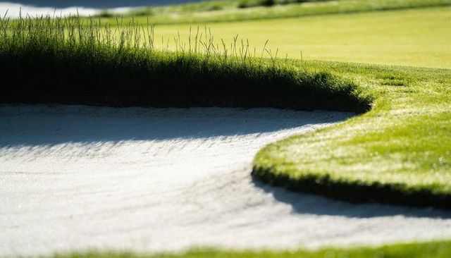 Sunlit golf bunker showing crisp turf lip and textured white sand with dramatic shadows