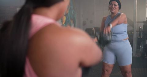 Two women partner kettlebell swing training in gym celebrating strength and teamwork