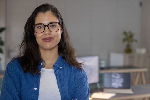 Confident young professional wearing glasses in modern office with laptop and monitors portrait