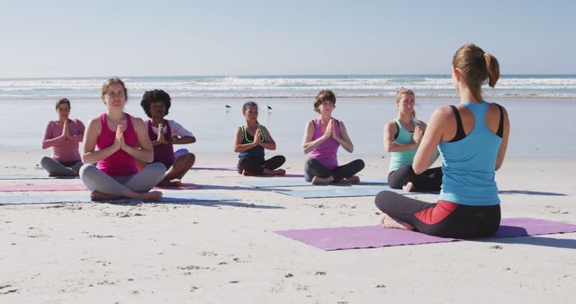 Group of diverse individuals practicing yoga on beach, guided by instructor. Suitable for promoting wellness, fitness events, meditation retreats, outdoor activities, health lifestyle content.