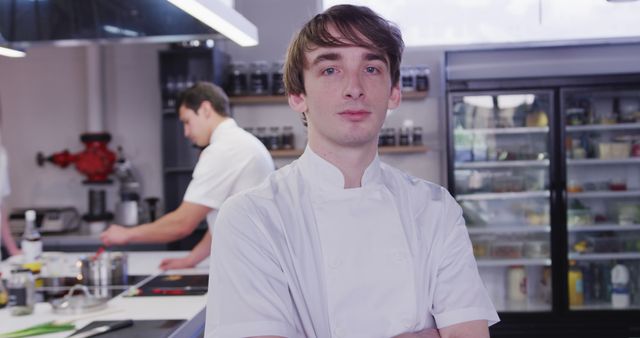 Young chef posing confidently with arms crossed in a gourmet kitchen, showcasing modern restaurant kitchen environment. Ideal for use in culinary blogs, restaurant websites, cooking class promotions, and hospitality industry materials.