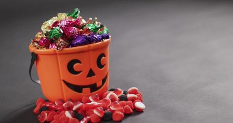 Halloween jack o'lantern candy bucket overflowing with wrapped chocolates and gummies