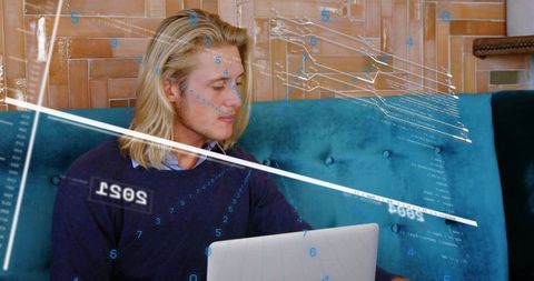 Casual young man analyzing laptop data with futuristic digital interface overlays on sofa