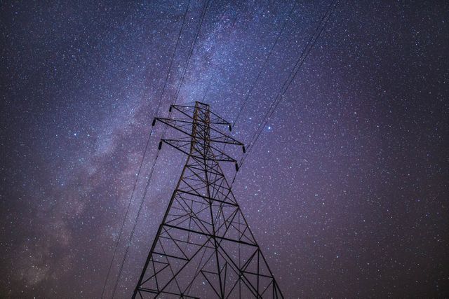 This image features a transmission tower silhouetted against a starry night sky with visible Milky Way. It can be used for illustrating themes related to electricity, urban infrastructure, technology, and the beauty of the night sky. It is perfect for websites, blogs, or educational materials dealing with astronomy, electrical engineering, and environmental sciences.