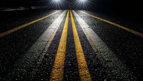 Glowing double yellow centerline reflecting under headlights on wet asphalt at night