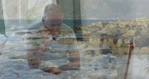 Contemplative senior man holding head with medication and cane, coastal waves overlay