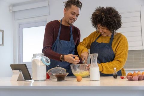 Couple baking together in modern kitchen wearing aprons mixing batter and smiling