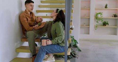 Young couple relaxing on floating staircase, sipping coffee in modern plant-filled interior