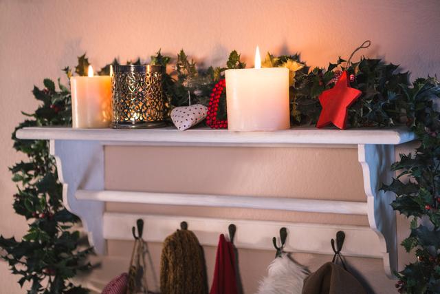 This image showcases a cozy Christmas decor setup with lit candles, festive garlands, and winter wear hanging on hooks. Ideal for holiday-themed content, home decor inspiration, and seasonal greeting cards.