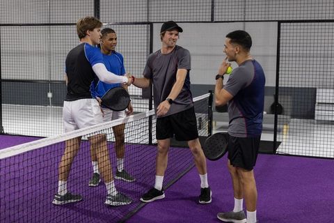 Padel doubles teams shaking hands at net on indoor purple court, sportsmanship and teamwork