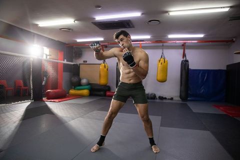 Shirtless mma fighter throwing punch in mixed martial arts gym, intense sparring training