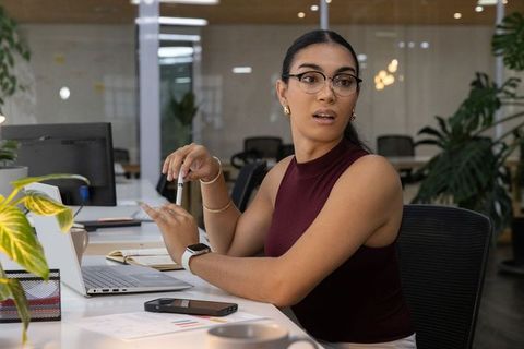 Young professional woman working at laptop and holding pen in modern open-plan office