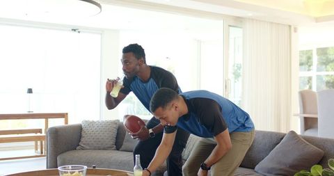 Friends watching football reaching for snacks holding pigskin in bright modern living room