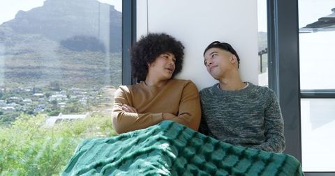 Friends relaxing under blanket on window seat with scenic view