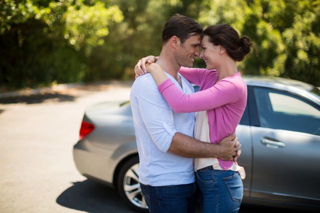 Young couple embracing near a car on a sunny day, showcasing love and affection. Ideal for use in advertisements for car brands, romantic getaways, relationship advice articles, or lifestyle blogs focusing on love and happiness.
