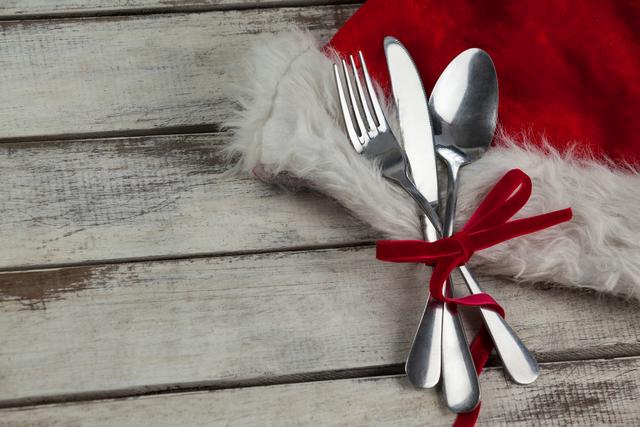 Cutlery set tied with a red ribbon placed on a rustic wooden table, evoking a festive holiday atmosphere. Ideal for use in holiday-themed advertisements, Christmas dinner invitations, seasonal blog posts, and festive dining guides.