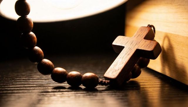 Wooden cross rosary resting on bedside table warm lamp light spiritual calm