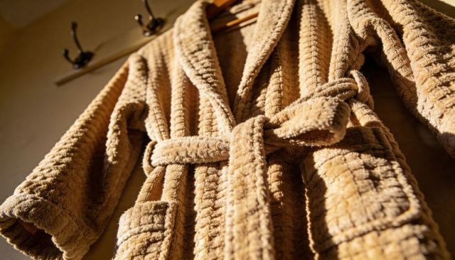 Beige waffle-textured plush bathrobe hanging on wooden hanger in warm cozy bedroom light