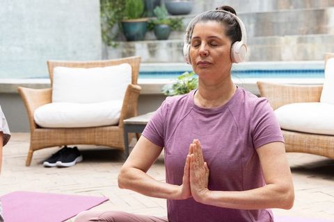 Mature woman meditating with headphones on poolside patio practicing mindful relaxation