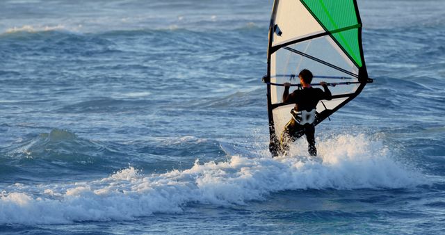 Individual enjoying windsurfing in the open ocean with vibrant waves and setting sun in background. Ideal for websites, brochures, or ads focusing on aquatic sports, outdoor adventures, or travel destinations.