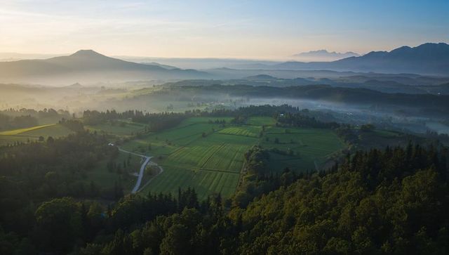 Sunlight casting warm glow over patchwork farmland and misty rolling hills at sunrise