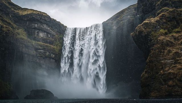 Misty plunge waterfall cascading between moss-covered cliffs over deep plunge pool