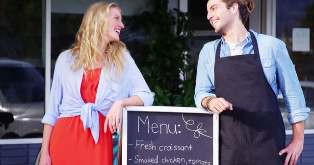 Smiling waiter and woman standing with menu board outside the cafe 4k