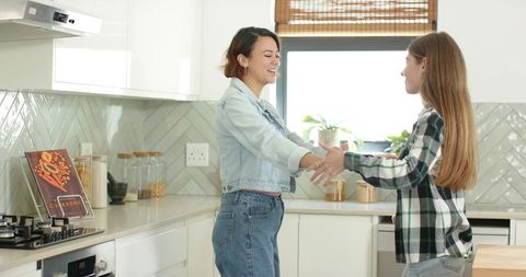 Mother and teen daughter sharing warm kitchen moment, smiling and reaching hands