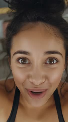 Vertical vlog: Young woman in sports bra smiling and speaking to camera while lying on bed