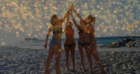 Friends celebrating on beach at sunset high-fiving in swimwear with golden bokeh lights