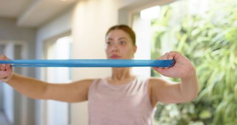 Female performing resistance band chest pull in sunlit hallway for home strength workout