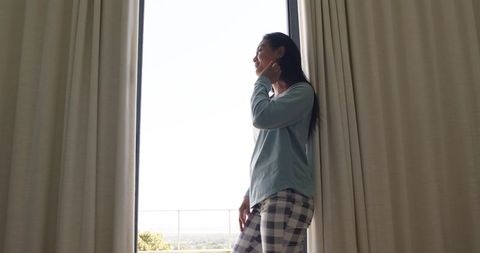 African american woman standing by glass door in plaid pajamas basking in morning light