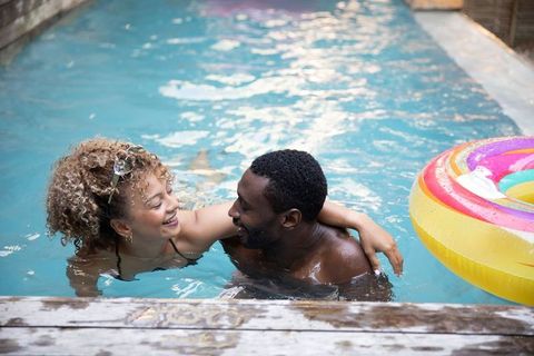 Diverse couple relaxing in pool embracing at wood edge with colorful donut float