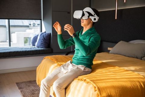 Young man wearing vr headset on bed interacting with virtual reality