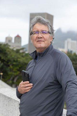 Senior man standing on urban terrace holding smartphone overlooking city skyline
