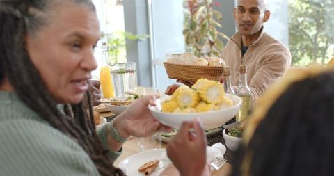 Sunlit multi-generational family sharing corn and bread around wooden dining table