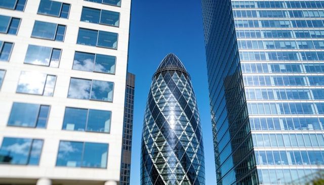 Iconic gherkin glass tower reflecting blue sky between modern high-rise offices