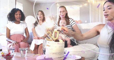 Women celebrating 30th birthday with cake and sparkler candles on cozy living room couch